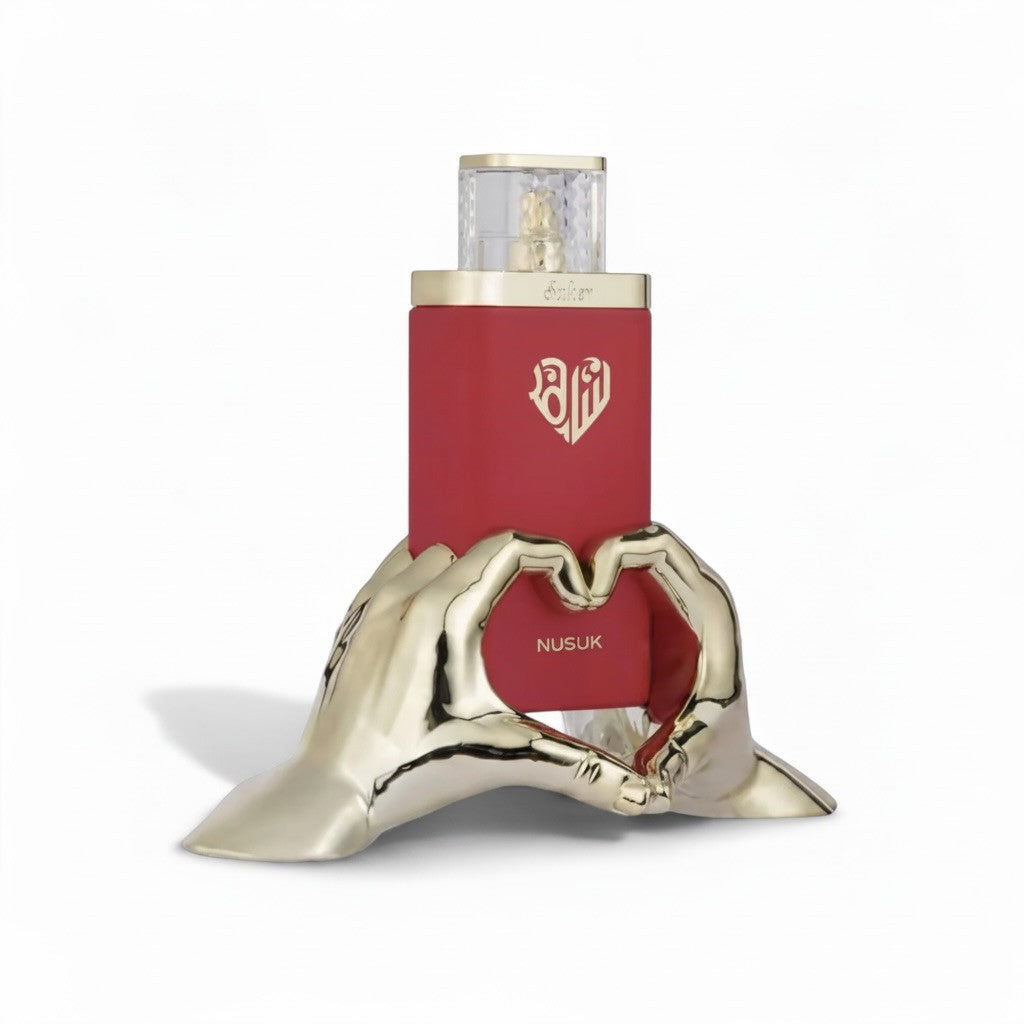Orijent Parfimerija Nusuk red Eau de Parfum bottle with gold heart emblem, held by gold hands forming a heart shape.